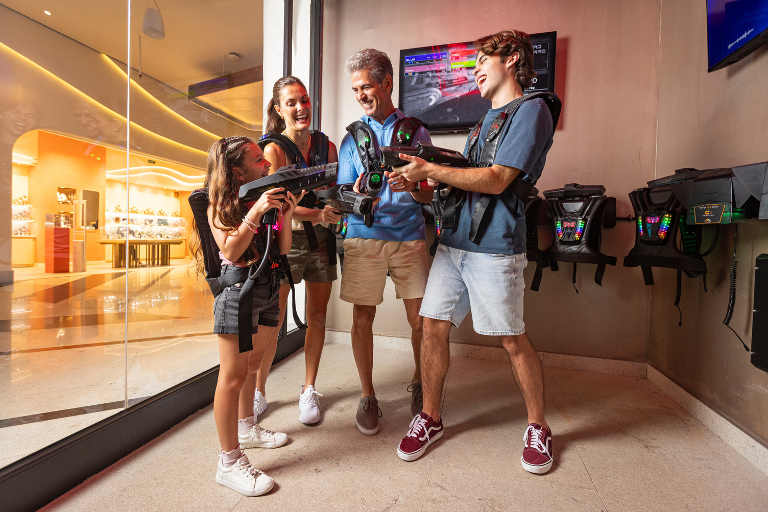 Family of four smiling and comparing laser tag scores in an indoor arena at AVA Resort Cancun.