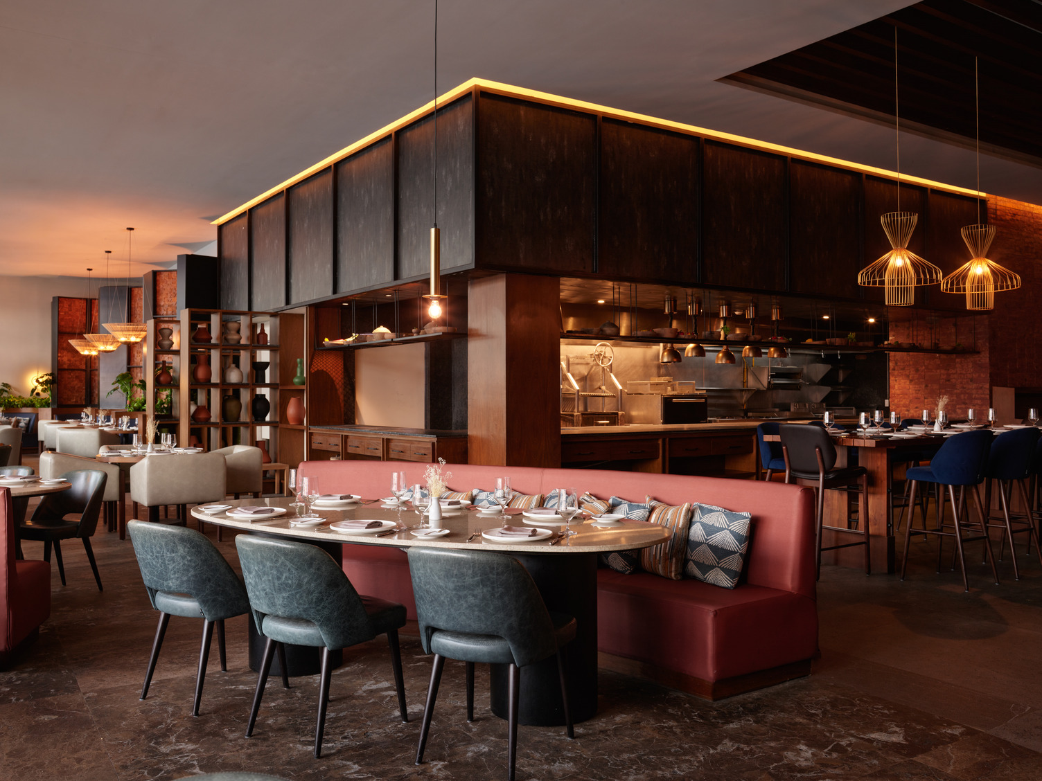Stylish restaurant interior with modern décor, red cushioned banquette seating, set tables, and open kitchen area.