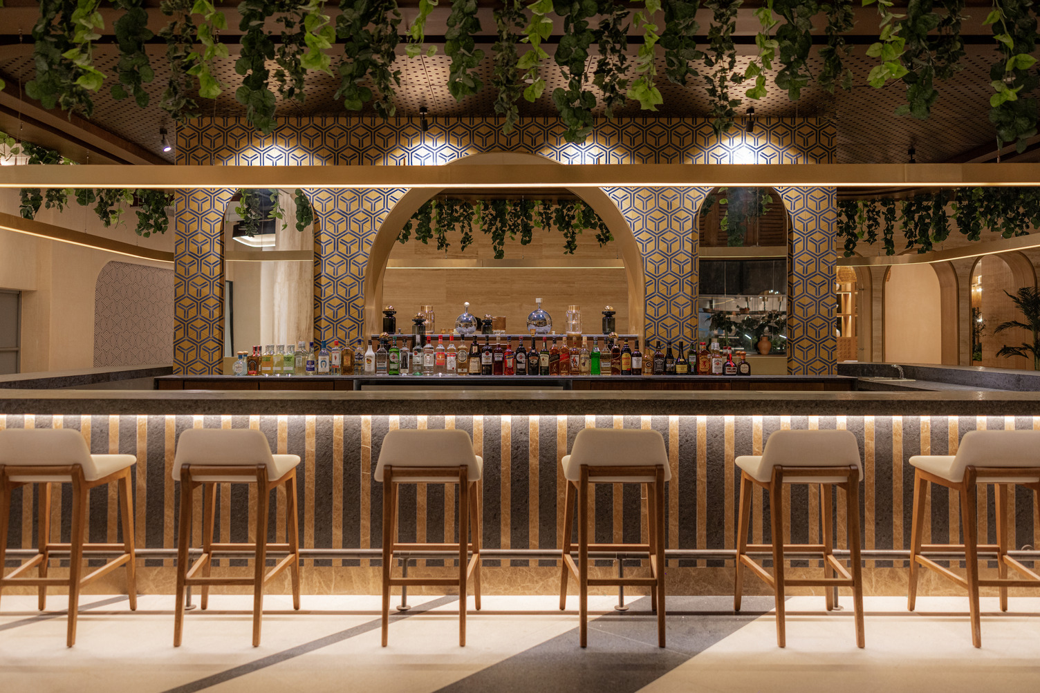 Stylish cocktail bar with a patterned backsplash, hanging greenery, and a row of bar stools in Cancun resort.
