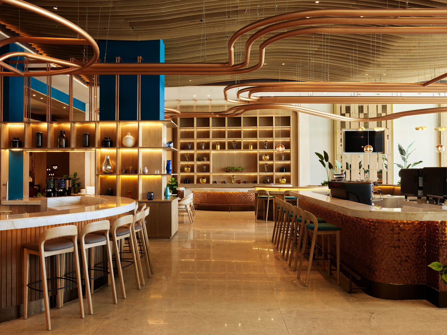 Modern hotel lounge with curved wooden accents, marble counters, bar stools, and warm ambient lighting.