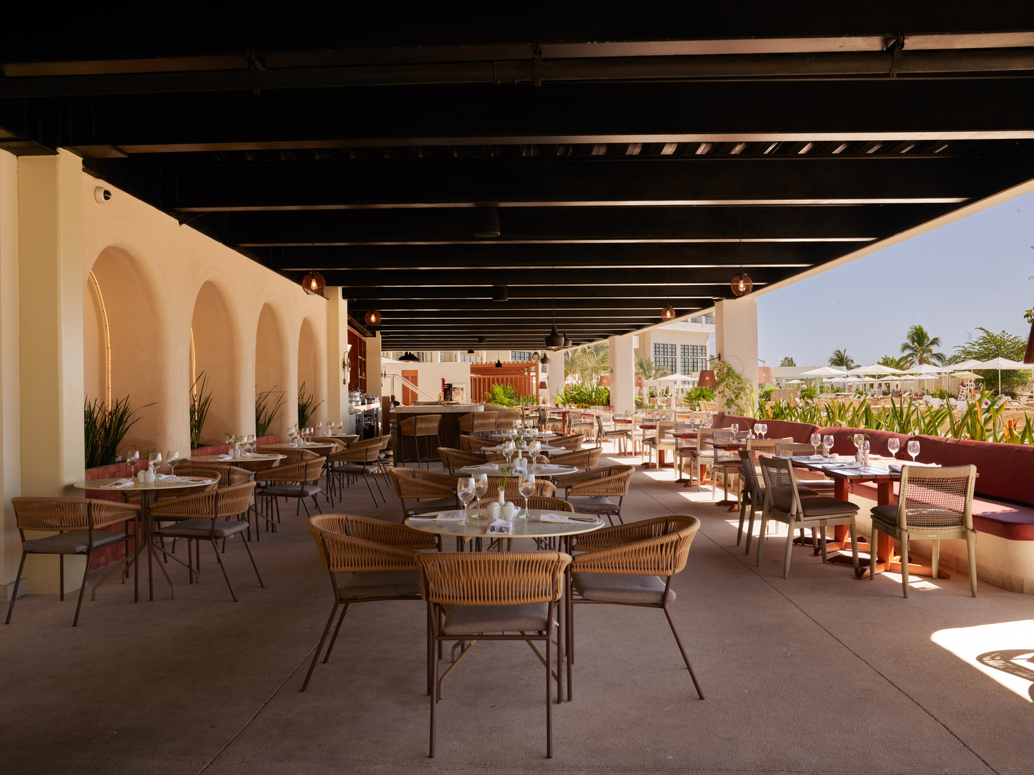 Outdoor dining area at AVA_AQUATICO_RESTAURANT with tables, chairs, and overhead beams, overlooking a sunny patio.