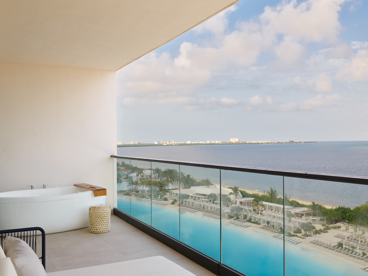 Balcony view from a suite with a hot tub, relaxing seating, and a panoramic ocean view overlooking a resort in Cancun.