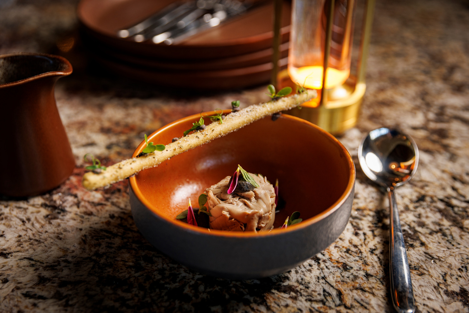 Elegant dish with gourmet presentation featuring delicately plated food and garnished with herbs, set on a speckled surface.