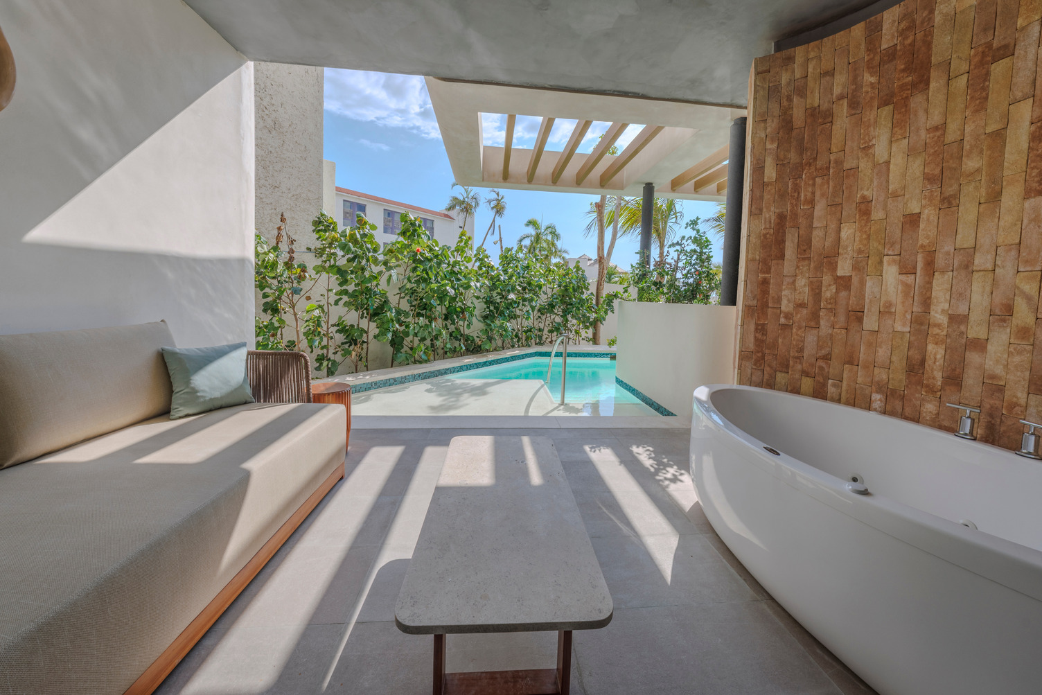 Luxury suite terrace with sofa, table, outdoor bathtub, and swim-up pool surrounded by greenery and modern design.