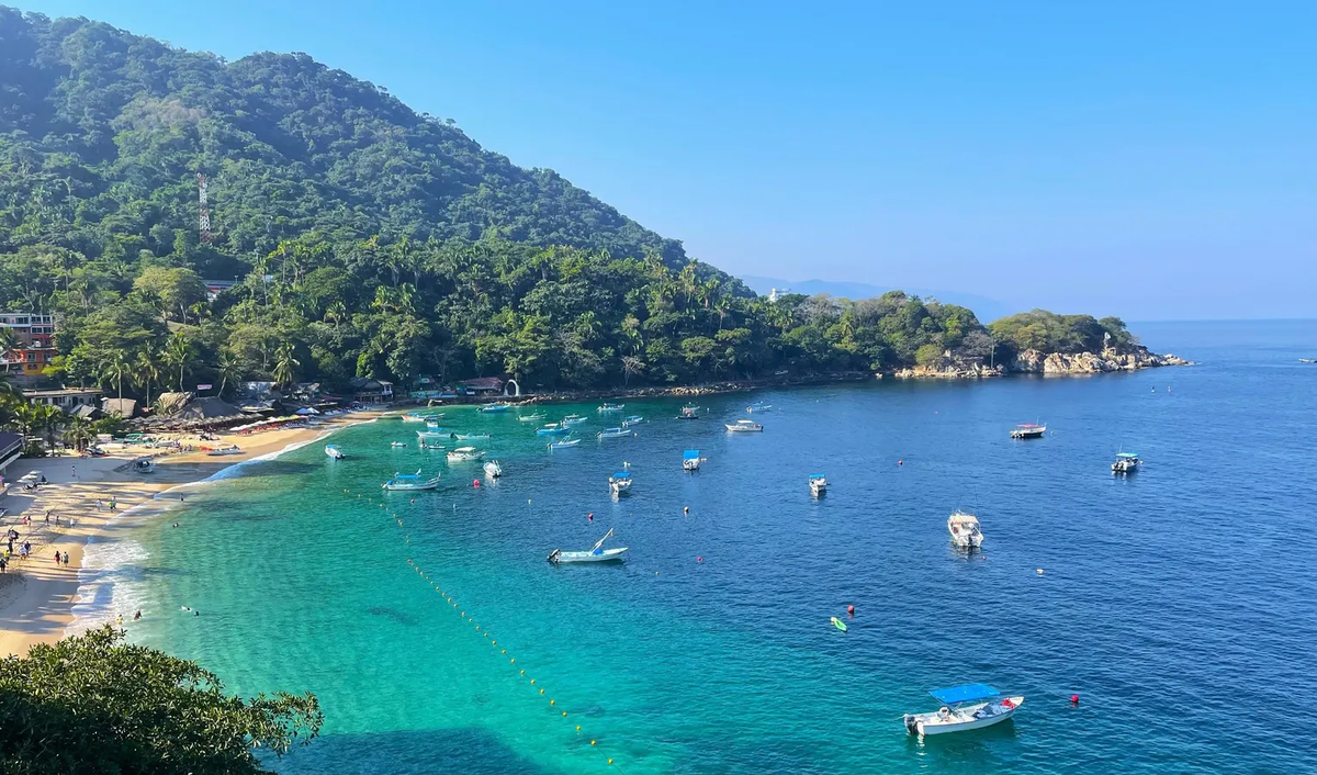 Riviera Nayarit coastline with green mountains, turquoise water, sandy beach, and boats floating offshore.