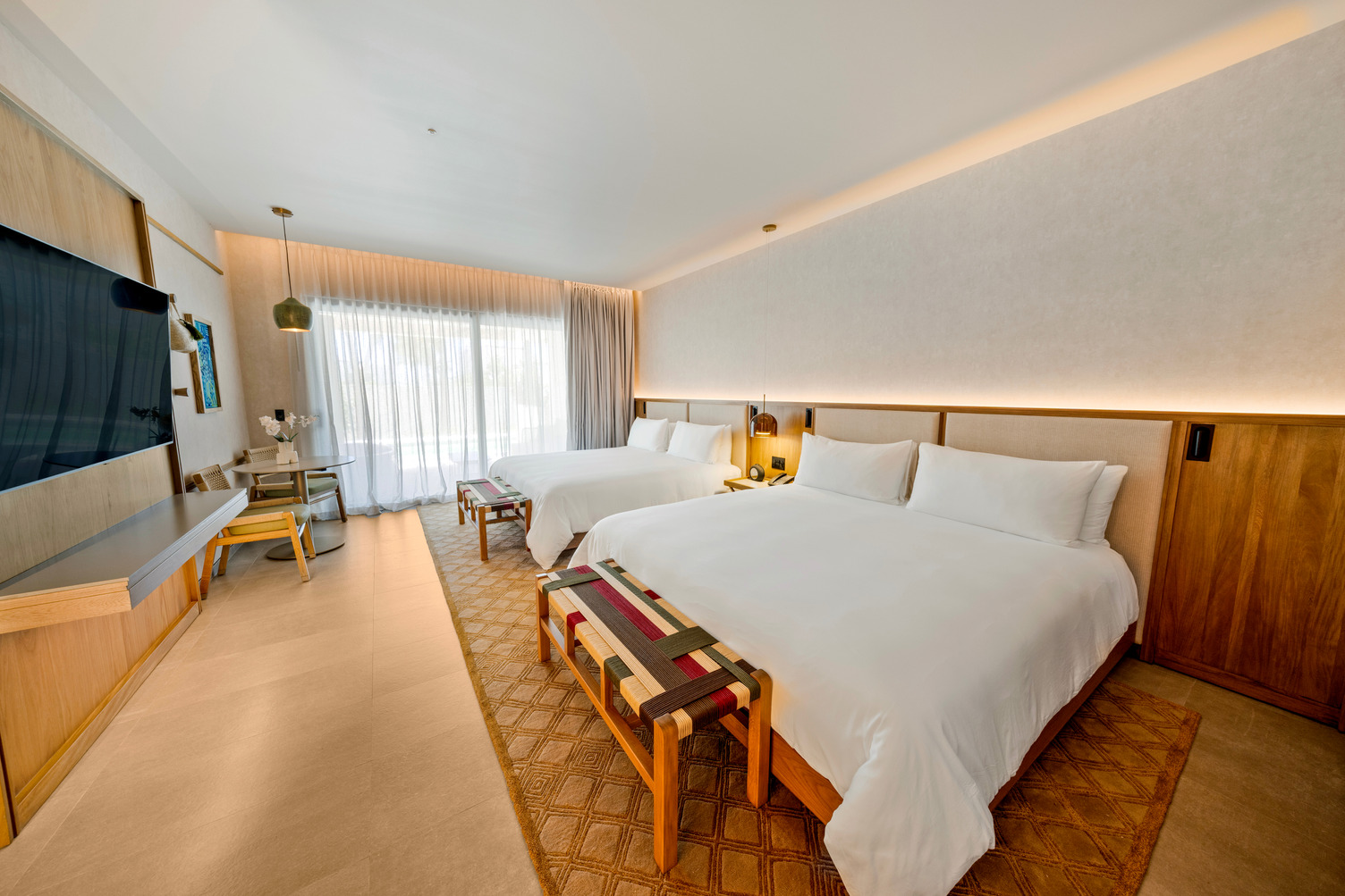 Spacious hotel room with two large beds, wood accents, TV, desk, and glass doors leading to an outdoor area.