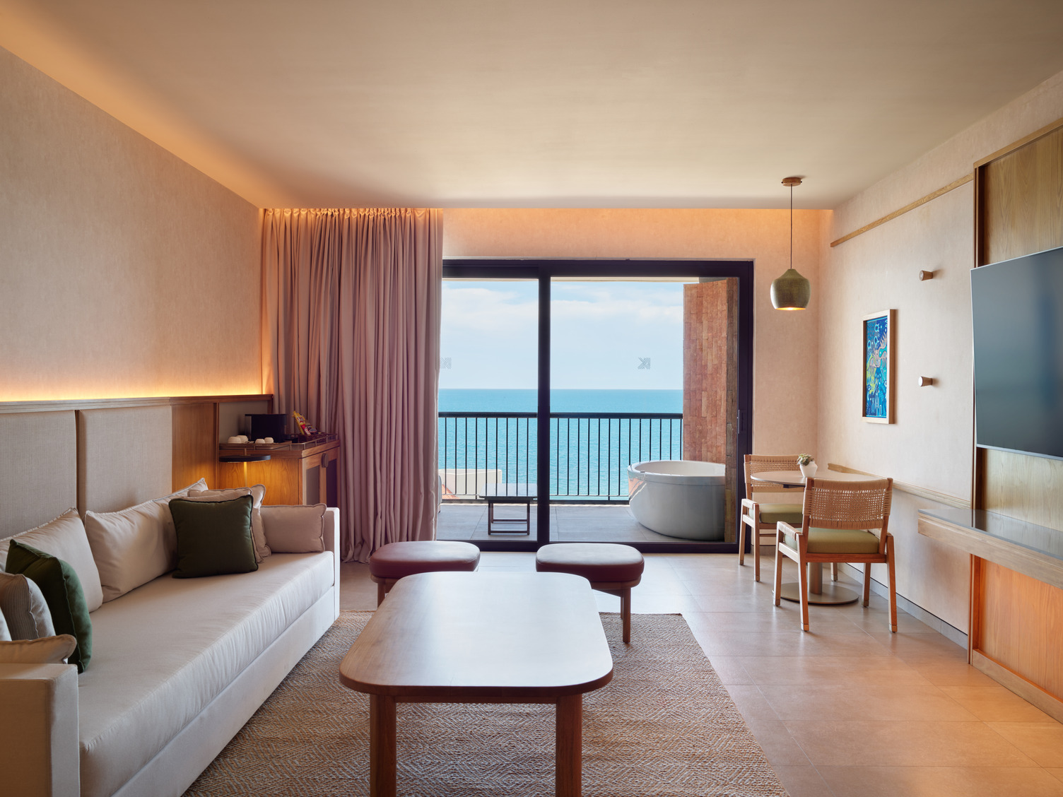 Spacious suite with ocean view, sofa, coffee table, balcony with hot tub, and modern decor.