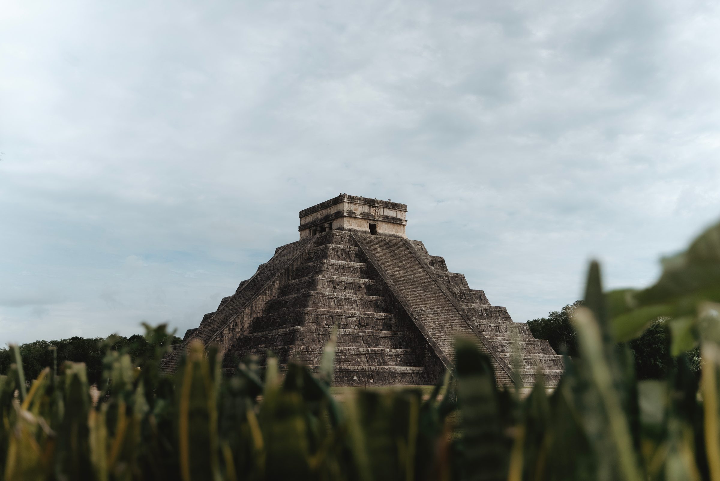 Pirámide antigua en Chichen Itza rodeada de vegetación bajo cielos nublados.
