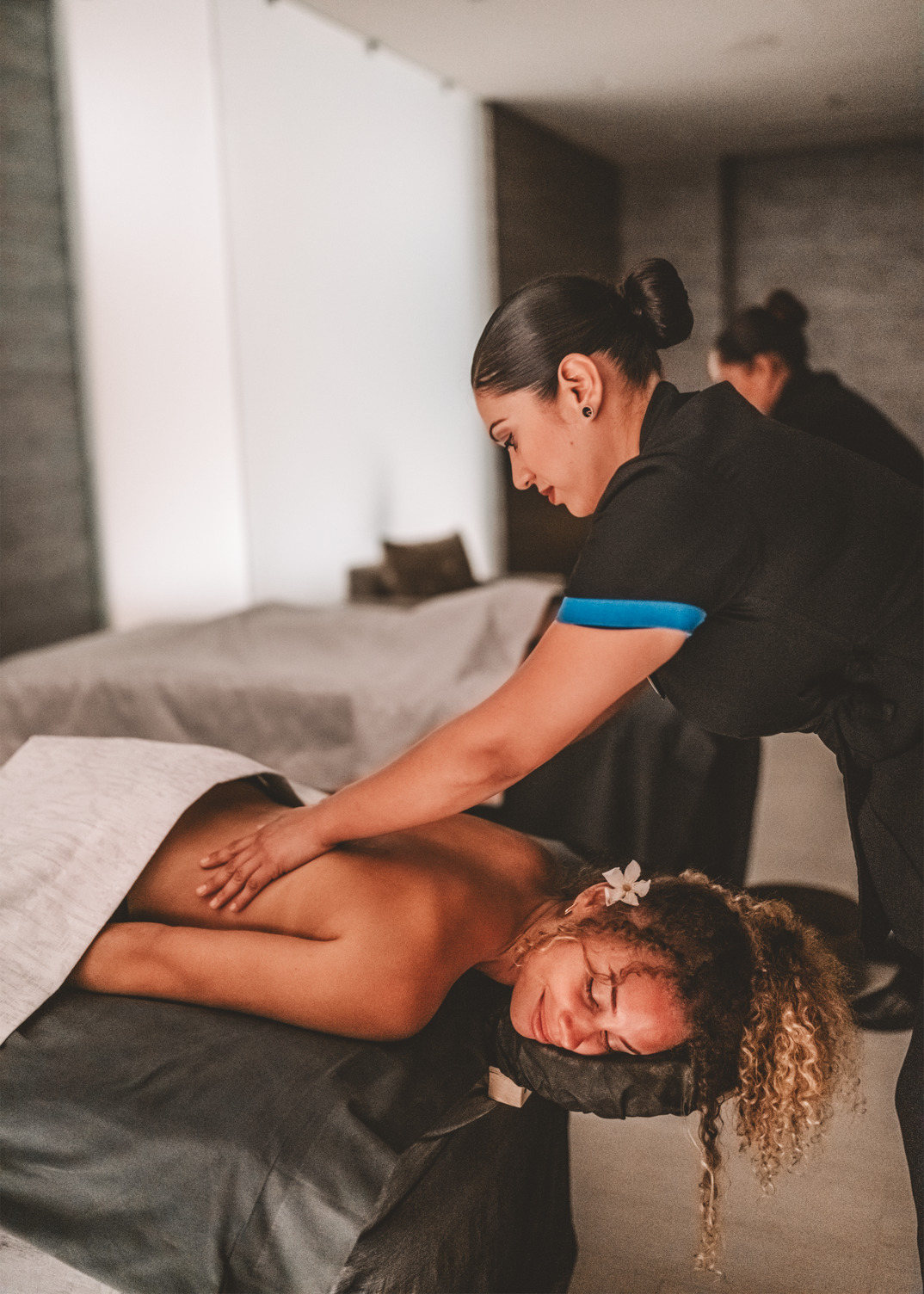 Persona recibiendo un masaje de espalda en un entorno de spa sereno, con una flor en el cabello, rodeada de iluminación suave