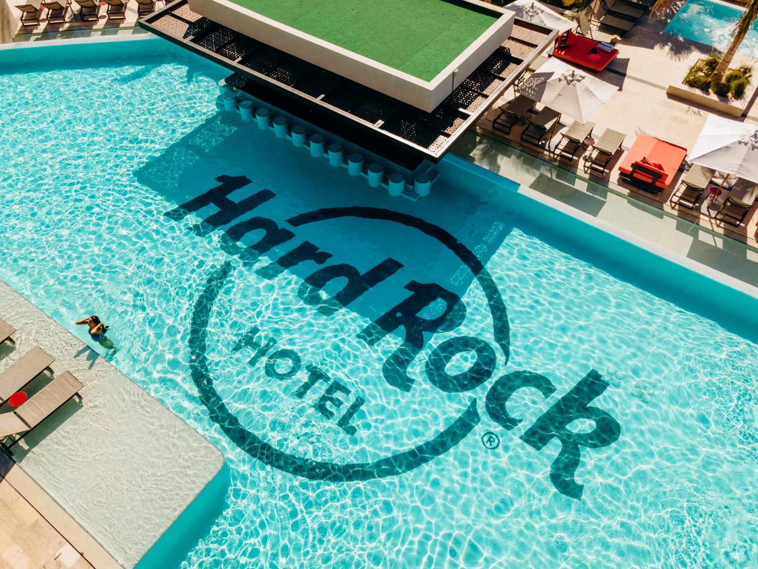 Aerial view of Eden Pool at Hard Rock Hotel, featuring lounge chairs, parasols, and a central swim-up bar.