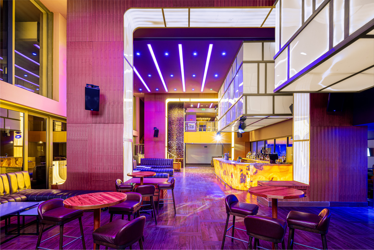 Bar salón vibrante con iluminación morada y amarilla, asientos modernos y barra iluminada.