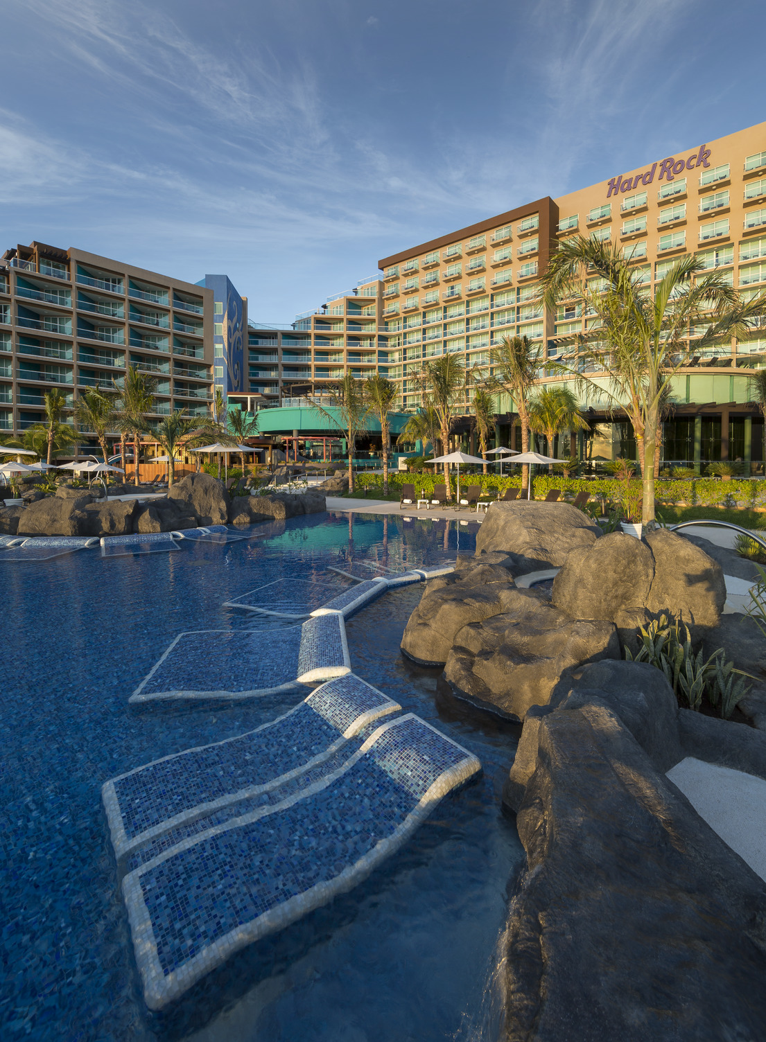 Poolside view at Hard Rock Hotel Cancun featuring lounge chairs in a luxurious pool surrounded by palm trees.