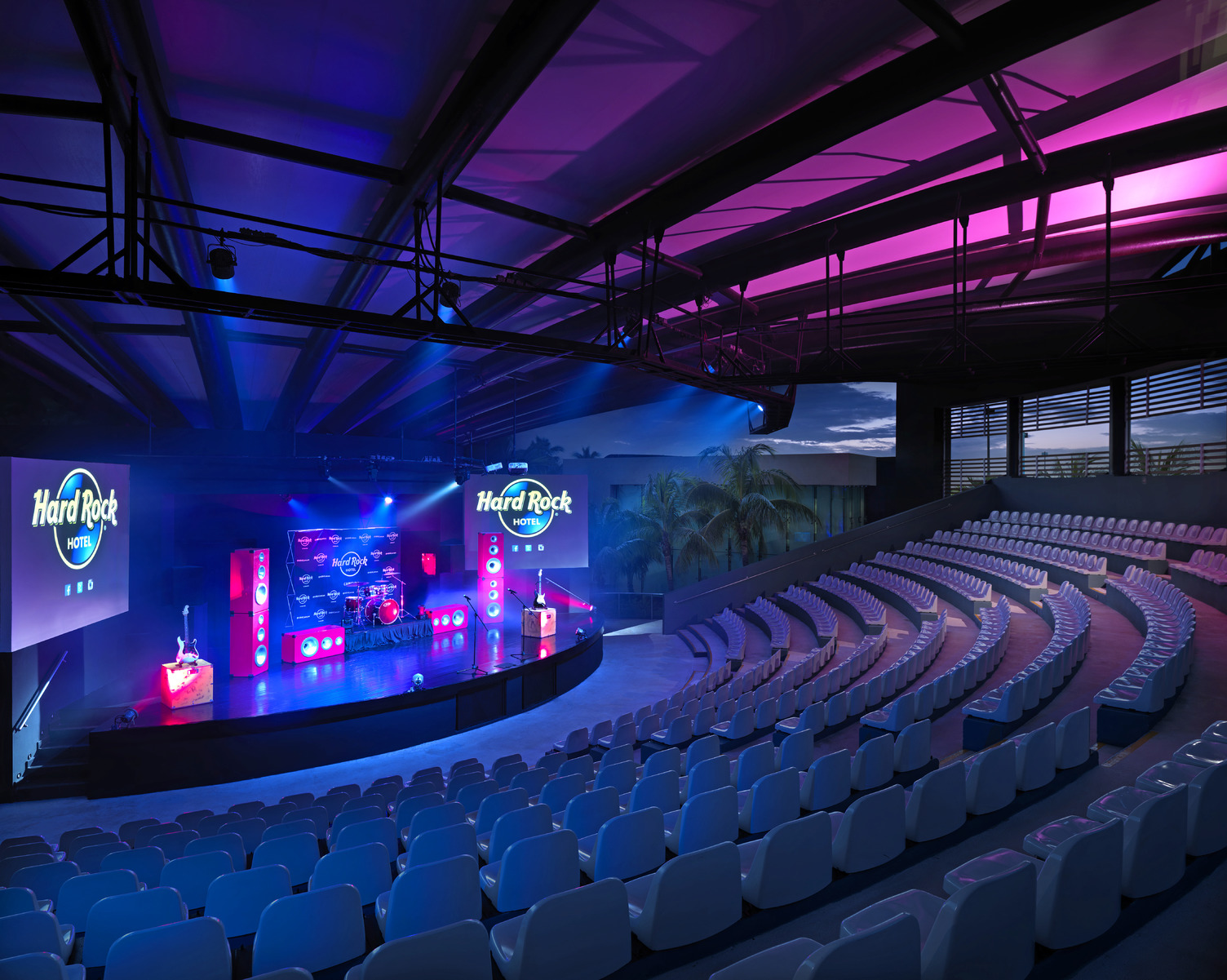 Anfiteatro del Hard Rock Cancún con asientos vacíos, escenario iluminado y vibrantes luces rosa y azul.
