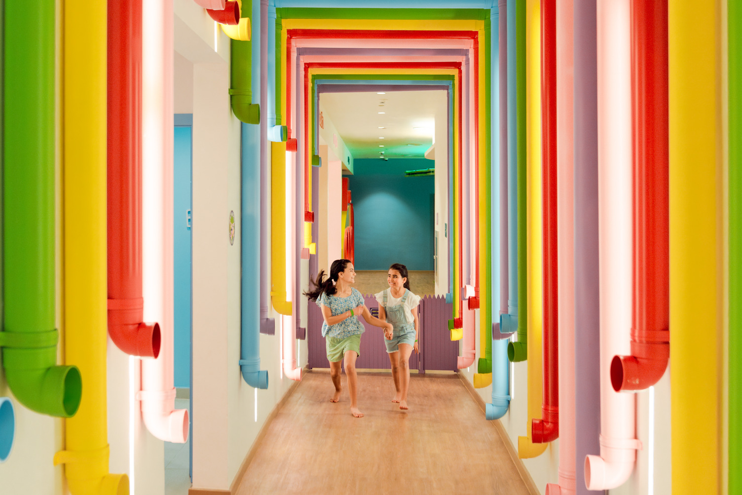 Two children playing in a colorful, pipe-lined hallway at a resort.