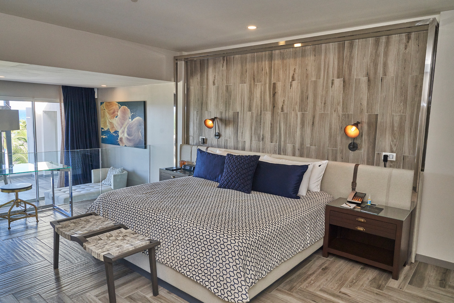 Habitación de hotel moderna con paneles de madera, acentos azules, área de descanso, arte en la pared y grandes ventanas con 