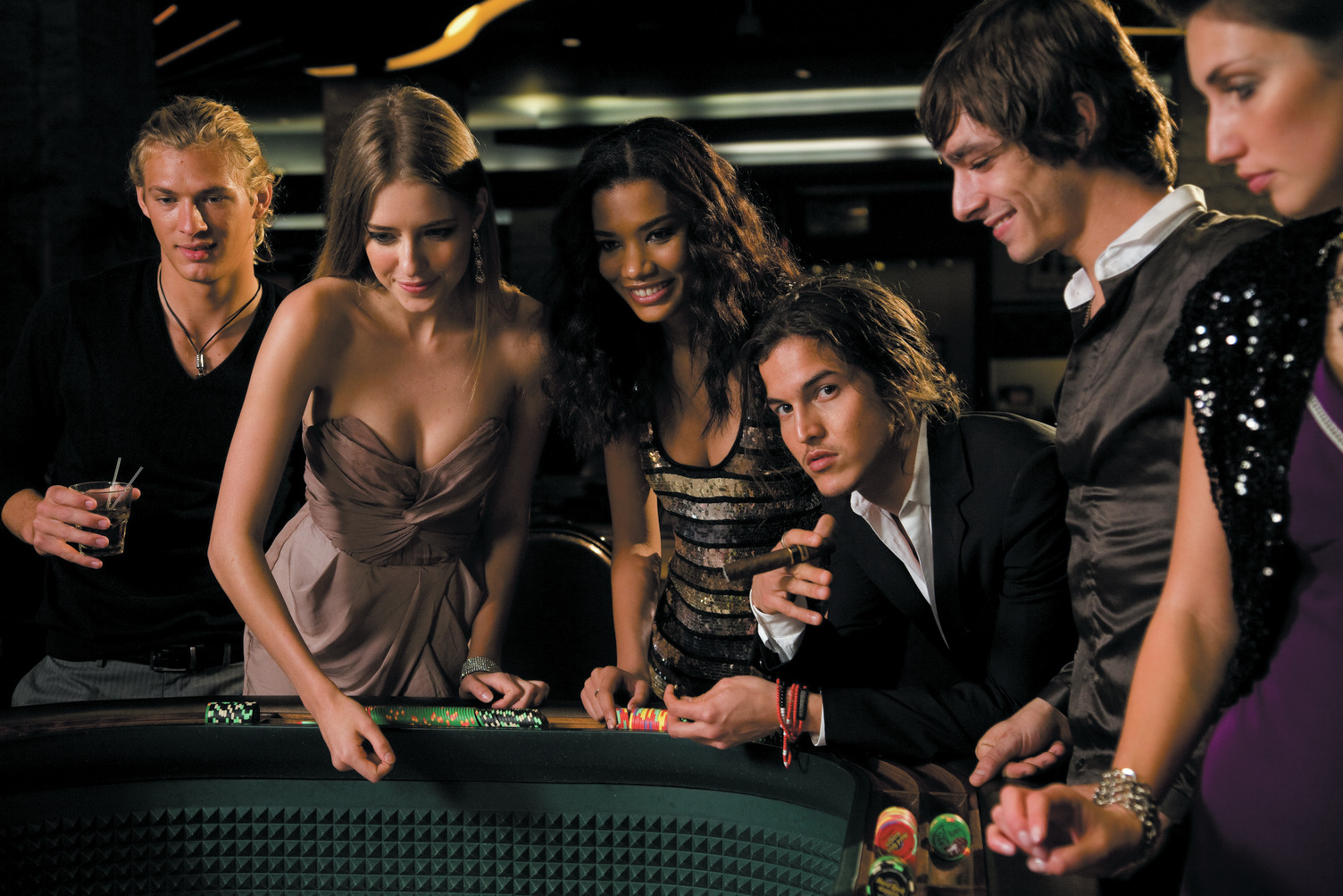Group of people enjoying a night at a casino table, engaged in a game, with chips and drinks in hand.