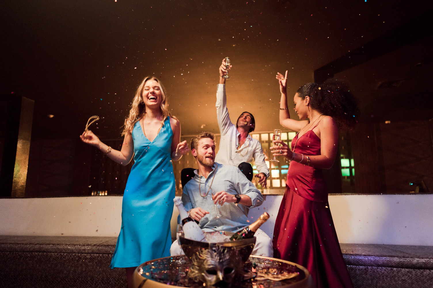 People celebrating at a club with drinks, wearing elegant attire, and surrounded by sparkles and colorful lights.
