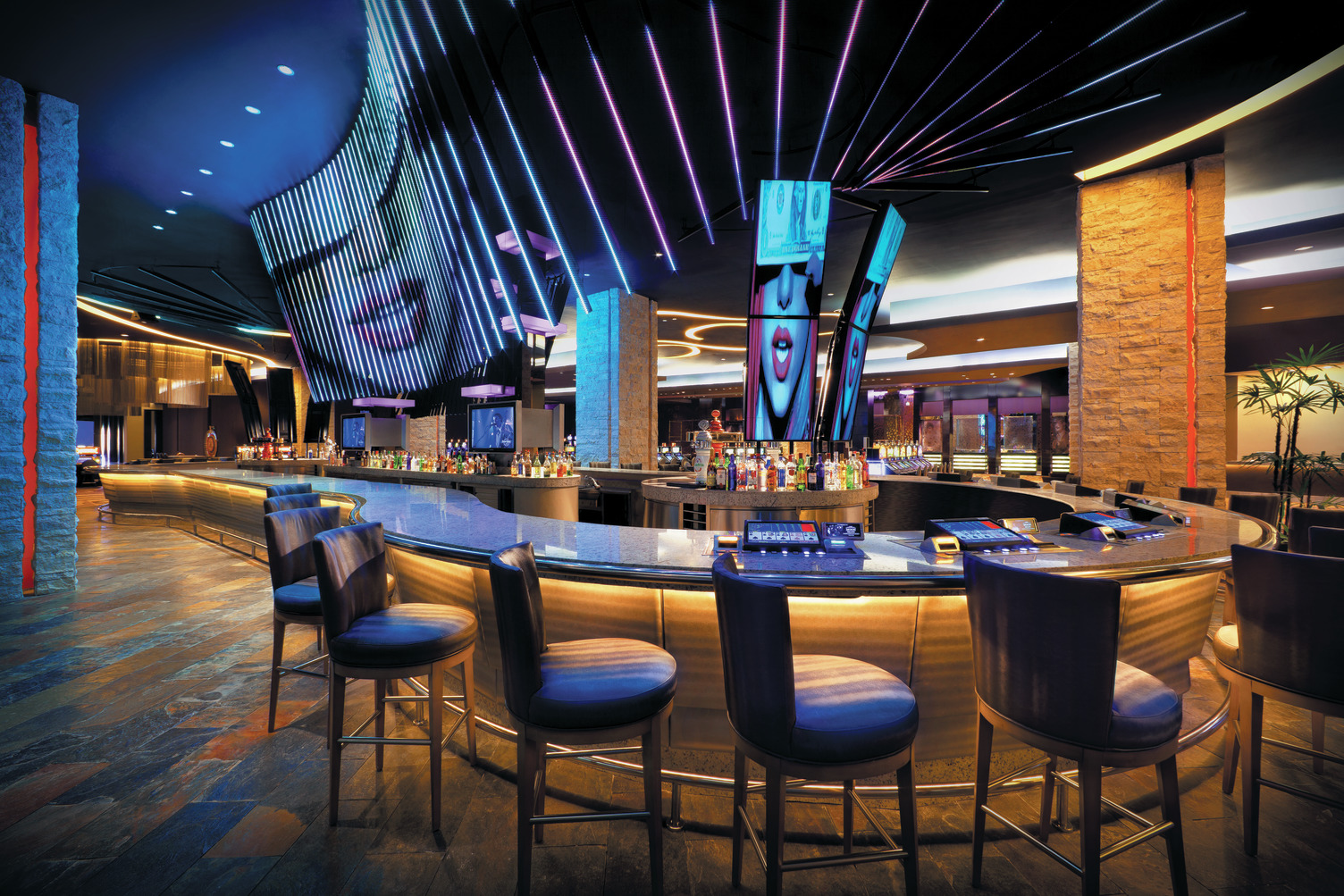 Modern bar with illuminated ceiling, curved counter, high stools, and abstract art at HRH Punta Cana Center Bar.