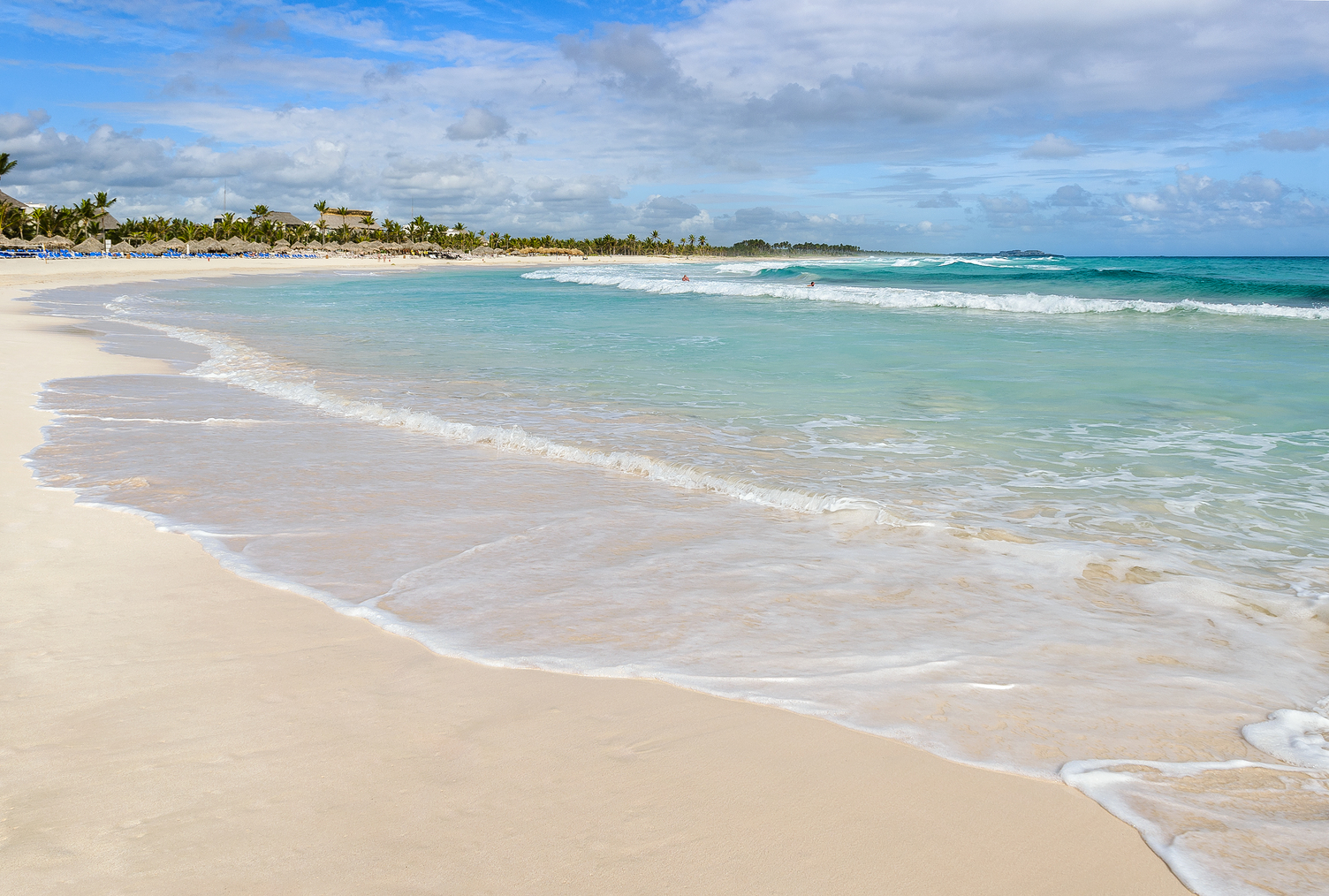 Sandy beach with gentle waves and turquoise water under a partly cloudy sky at Punta Cana.