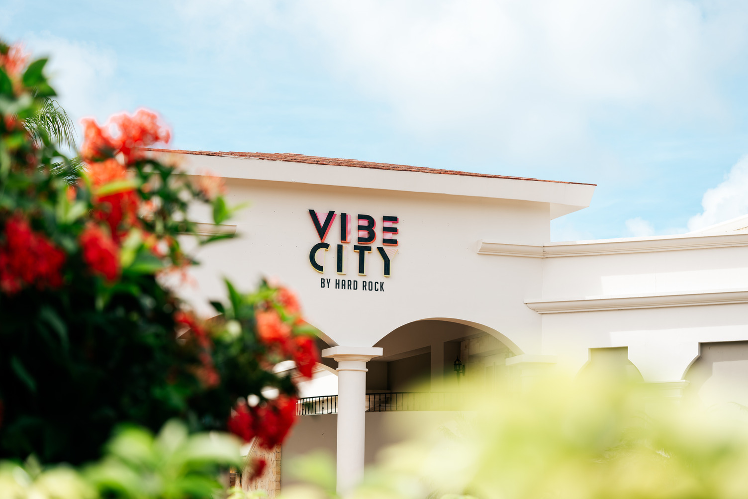 Entrada de Vibe City by Hard Rock, con arcos blancos y flores rojas en primer plano.