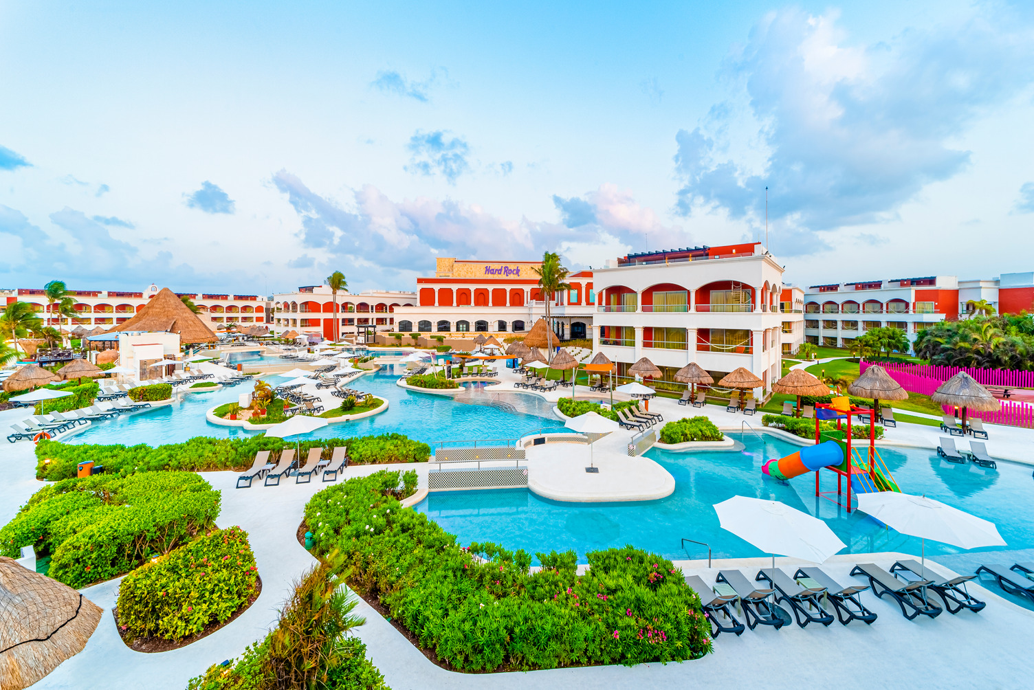 Amplia área de alberca en la sección Hacienda del Hard Rock Hotel Riviera Maya con camastros, área de juegos acuáticos y ciel