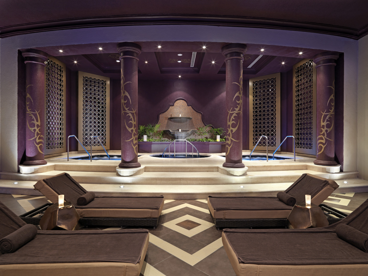 Luxurious spa hydrotherapy area with lounge chairs, purple pillars, and decorative walls at Hard Rock Riviera Maya.