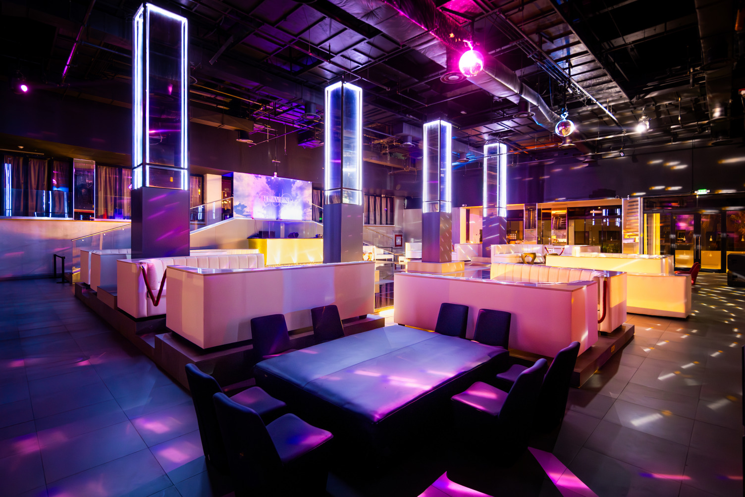 Interior vibrante de discoteca con columnas luminosas, iluminación de neón, mesas, sillas y pista de baile en Heaven Night Cl