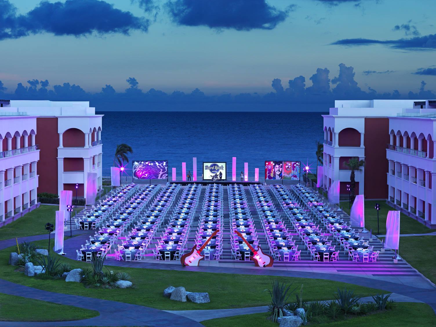 Woodstock Terrace setup with tables and chairs facing a large screen, set against an ocean backdrop in Riviera Maya.