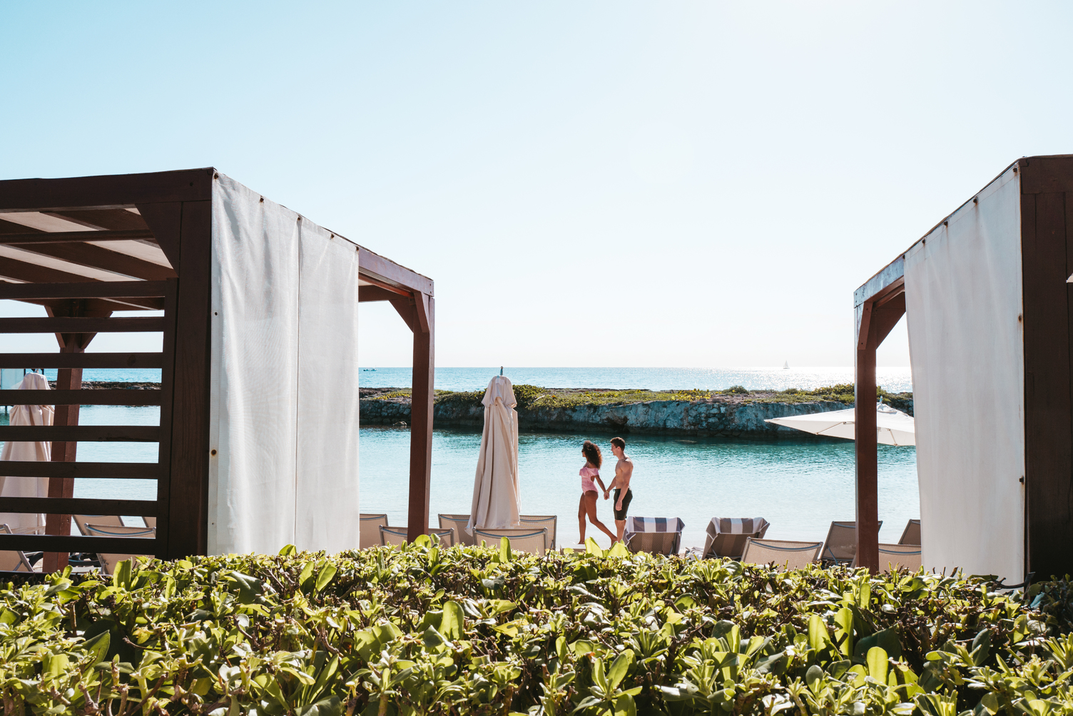 Pareja con un niño caminando por cabañas de lujo cerca de un paseo marítimo en un resort, con cielos azules despejados arriba