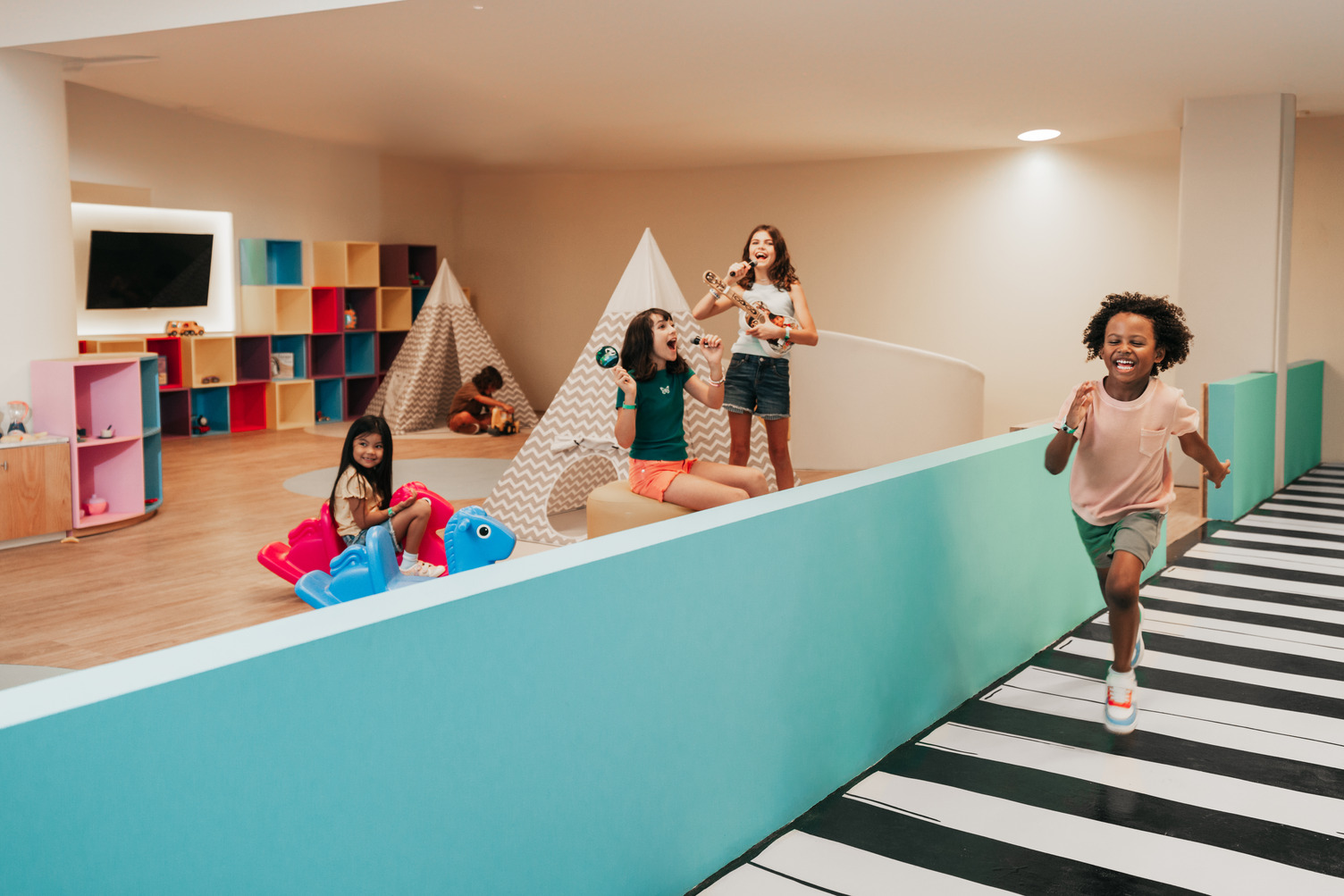 Niños jugando en Roxity Kids Club con tiendas, instrumentos musicales y juguetes coloridos en una sala de juegos vibrante.