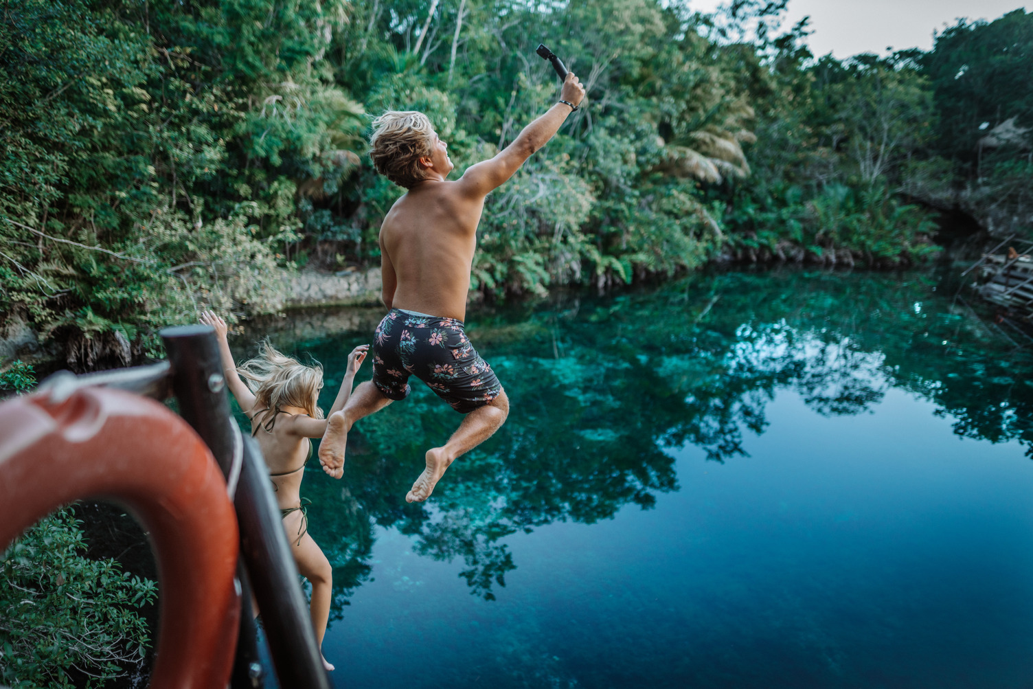 Dos niños saltando a un cenote rodeado de exuberante vegetación.