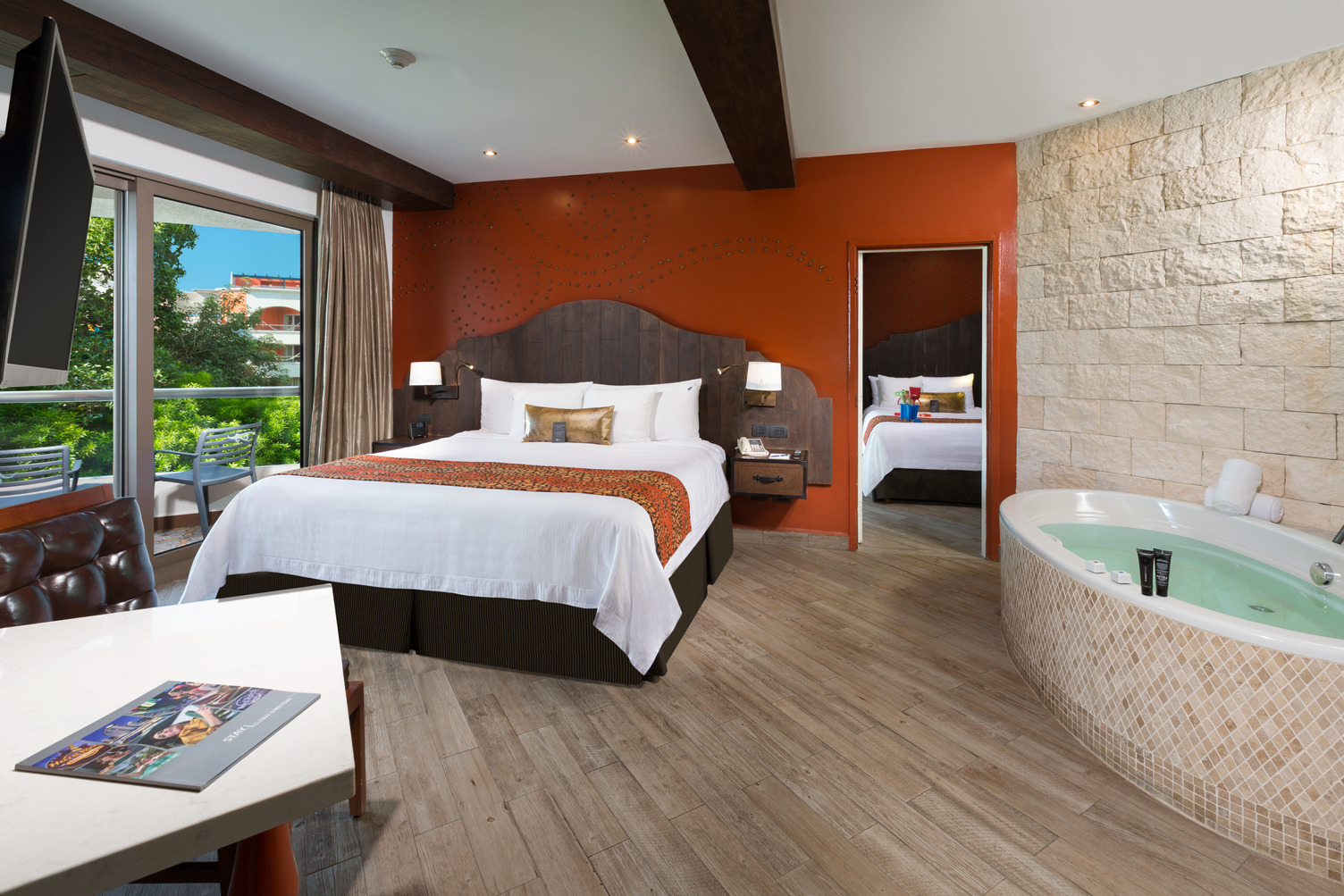 Amplia habitación de resort con una cama grande, jacuzzi, vista al balcón y detalles de madera en HRHRM Hacienda, México.