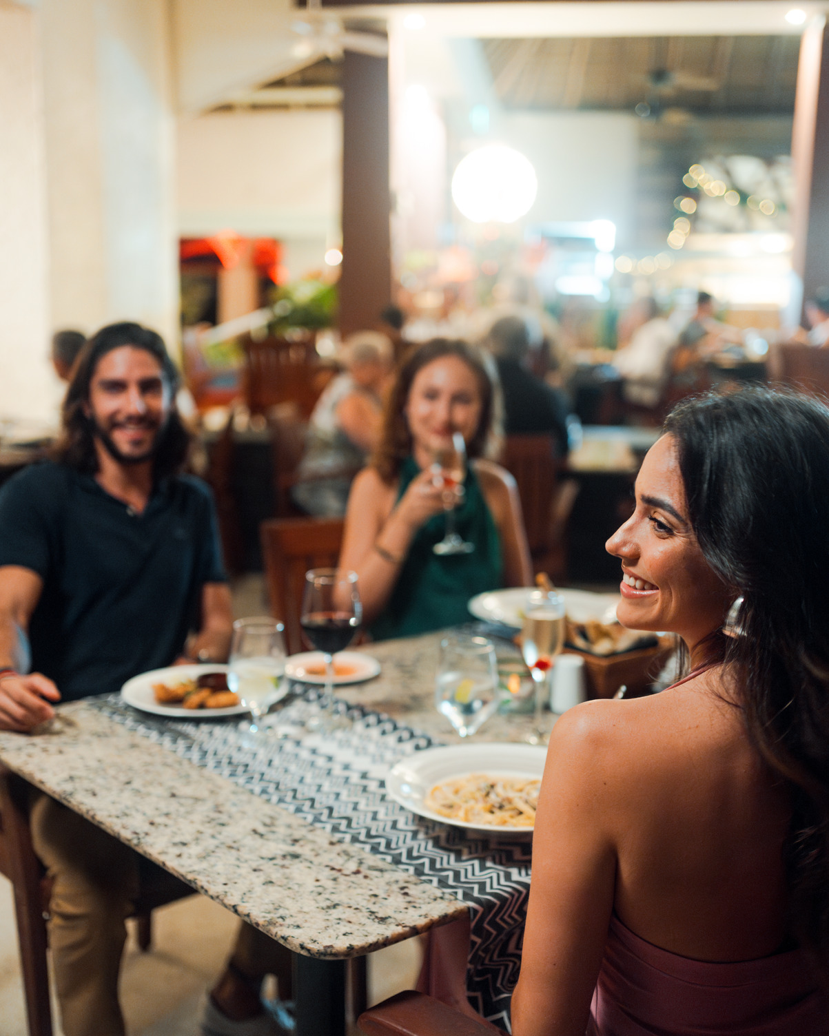 Group of people dining at a restaurant, sitting at a granite table with drinks and appetizers, backgrounds blurred.