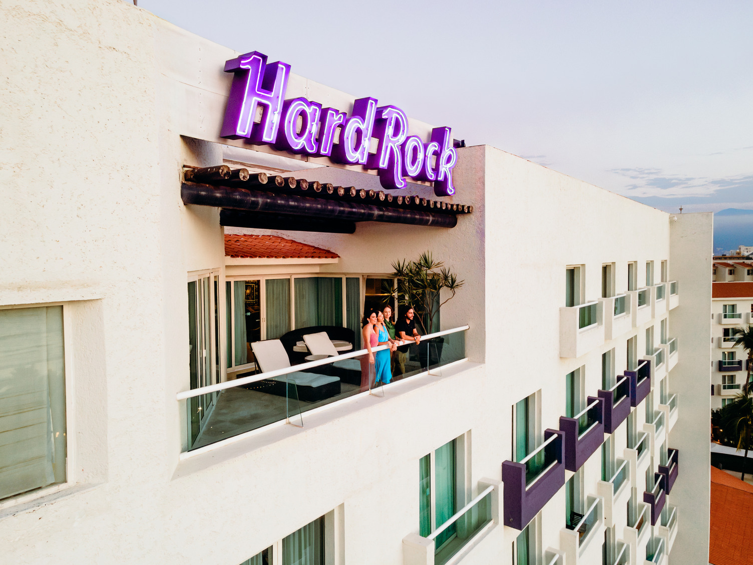 Hard Rock hotel exterior with purple sign, balcony view, and two people standing outside a suite in Puerto Vallarta.
