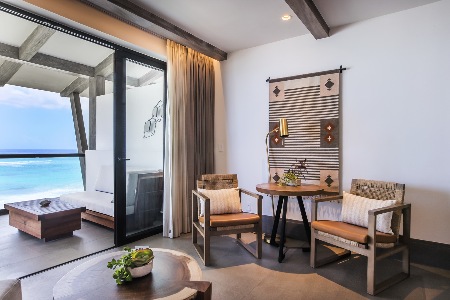 Interior elegante de la suite Alcoba con un acogedor área de estar, mesa de madera, sillas, y vista de la terraza hacia el oc