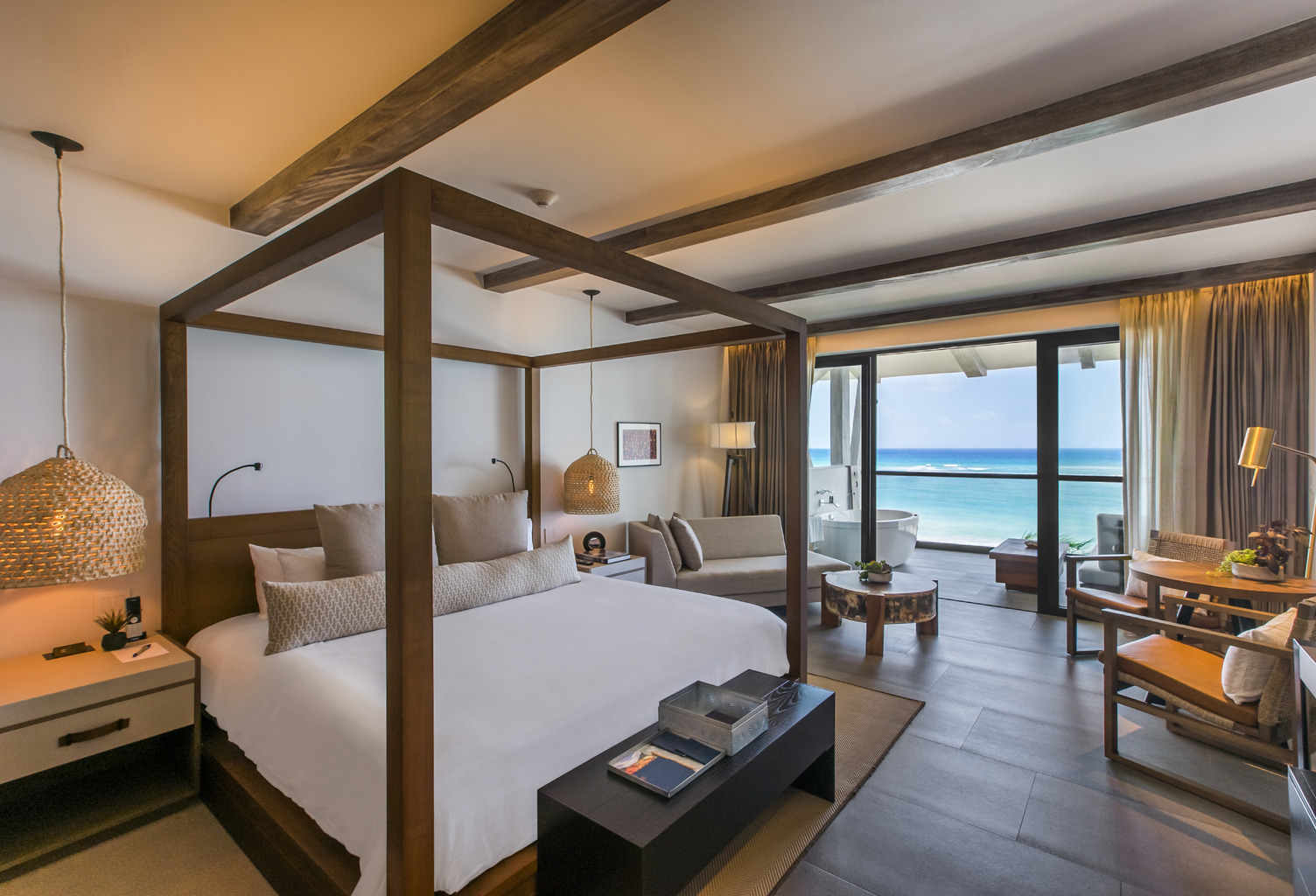 Espaciosa habitación de hotel con una cama con dosel, área de estar acogedora, y vista del océano a través de grandes ventana