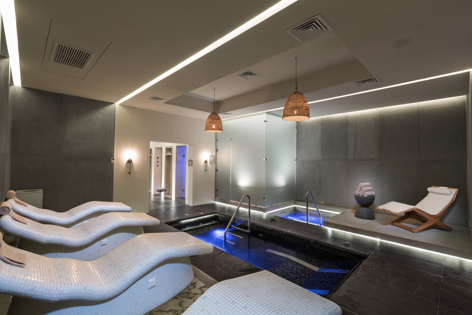 Spacious spa hydrotherapy area with lounge chairs, illuminated pool, and soft lighting, featuring modern decor.