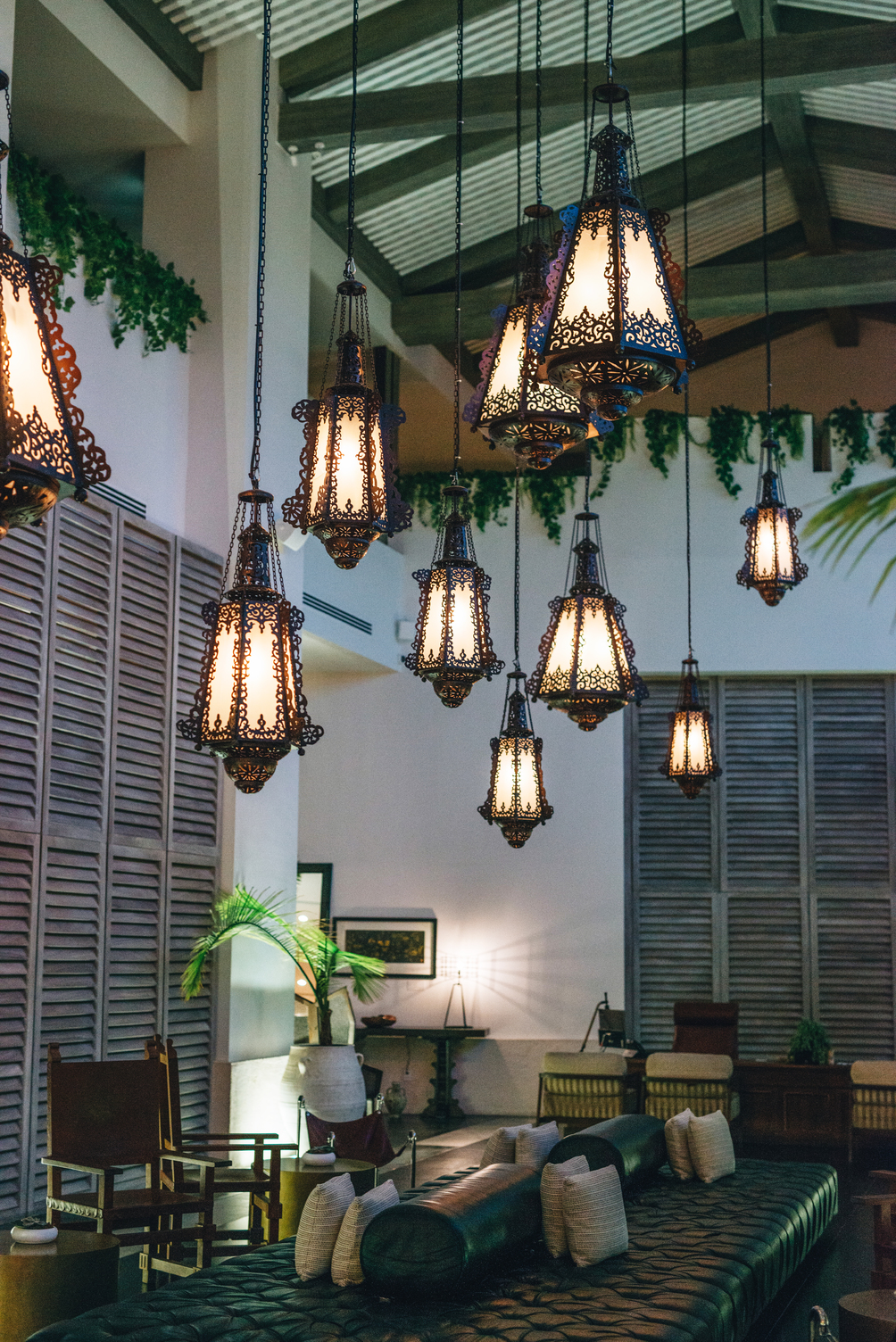 Faroles colgantes iluminan un elegante interior de resort con muebles de madera y acentos de vegetación exuberante.